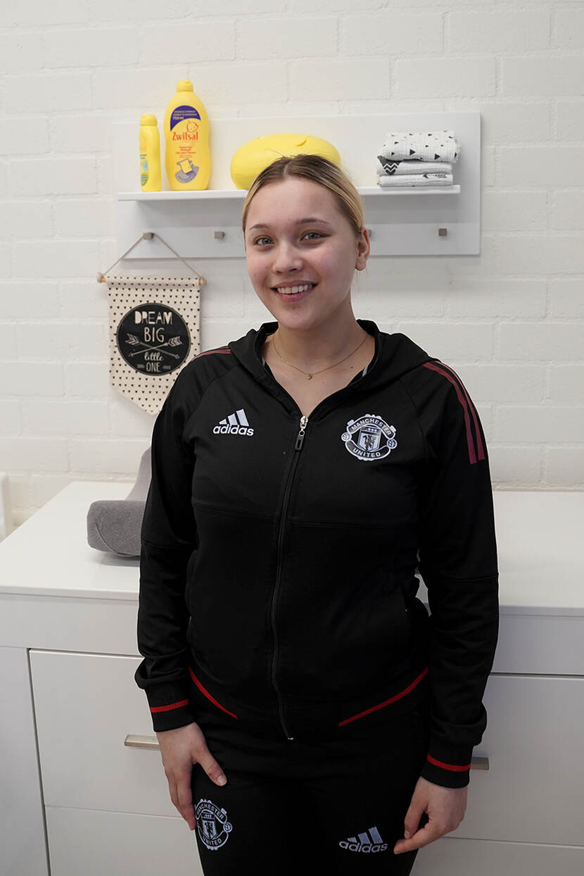 Brandee, een meisje in een zwart trainingspak, staat in het zorglokaal van haar school - Accent Praktijkonderwijs in Nijkerk. Ze kijkt glimlachend in de camera.